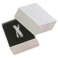 A white ring box with a ring inside, placed on a satin surface inside the box.