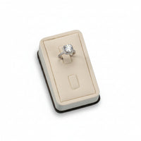 A chocolate and beige leatherette ring stand with a cushioned surface displaying a single ring on a white mount.