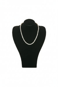A black velvet wide shoulder neck form displaying a strand of pearl necklaces.