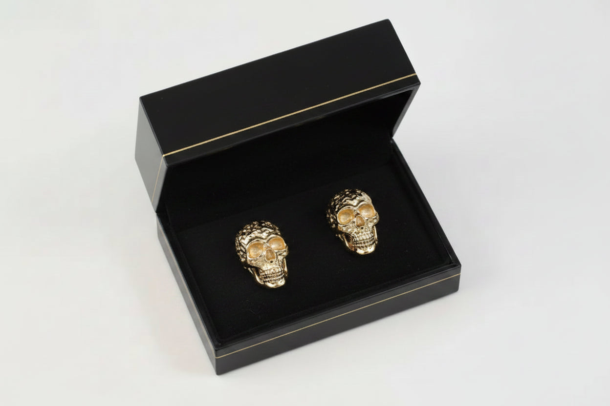 Gold skull-shaped earrings in an open black box