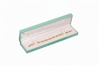 Gold bracelet in a green jewelry box on a white background