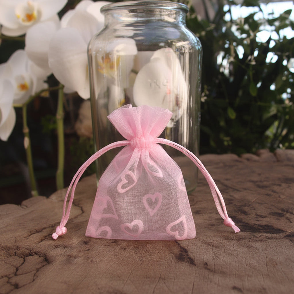 Two small drawstring bags, one pink and one red, with heart patterns on a wooden surface.